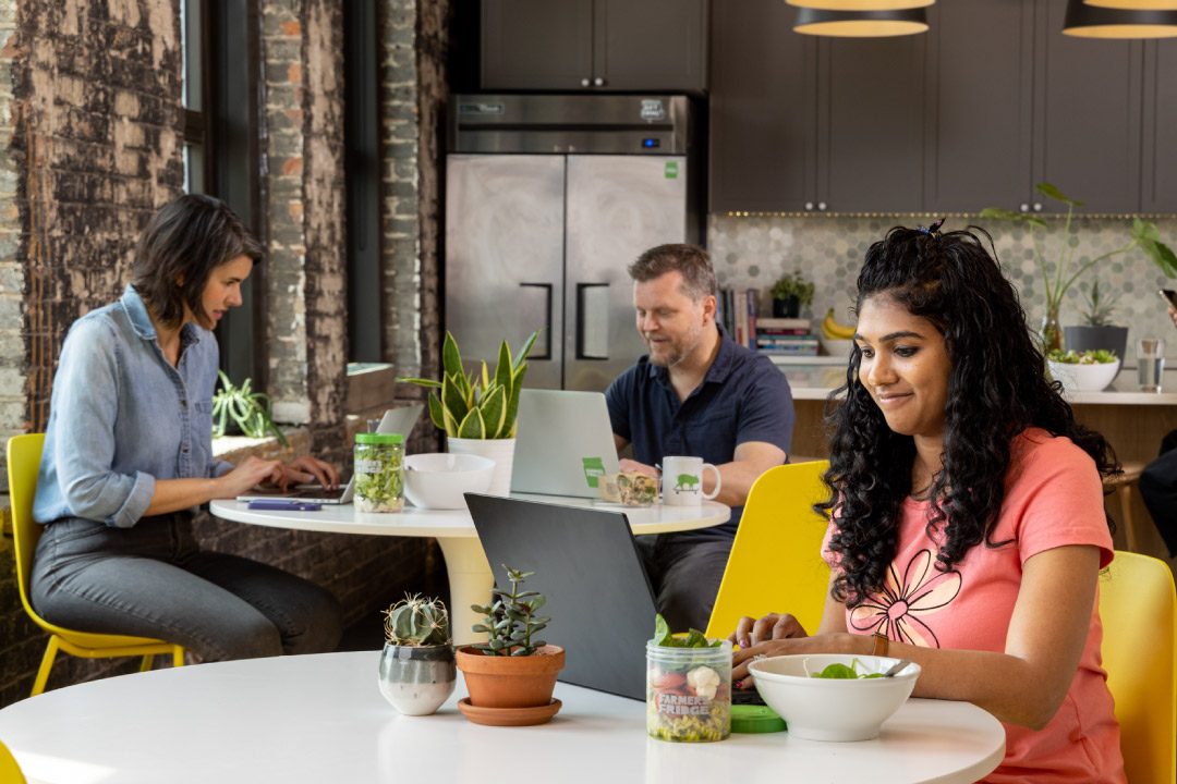 Multiple office workers eating at tables while enjoying Farmer's Fridge for lunch.