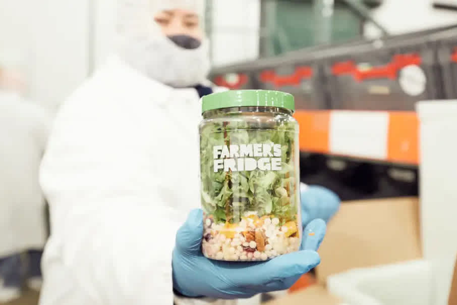 Farmer's Fridge worker holding up a Harvest Salad in a jar.