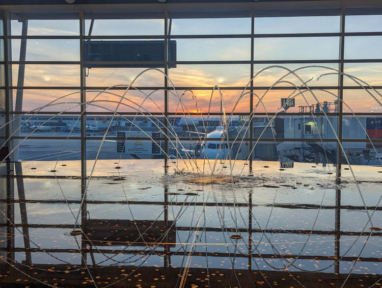 Photo of a fountain inside the Detroit airport with a plane on the tarmac in the background.
