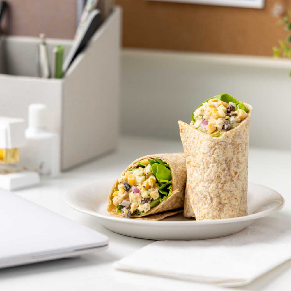 A Napa Chickpea Wrap served on a plate on someones desk at work. 