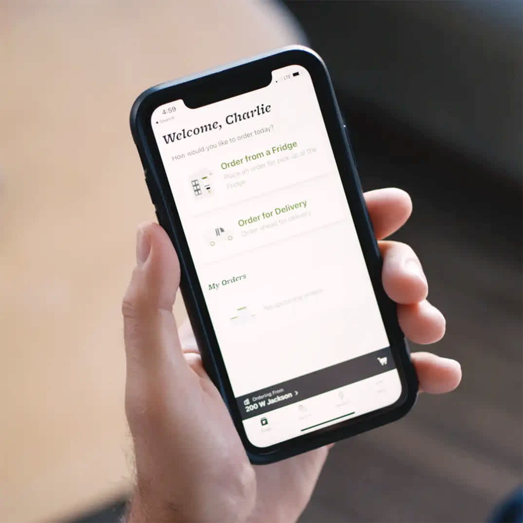 Image of a man holding a phone open on the Farmer's Fridge app.