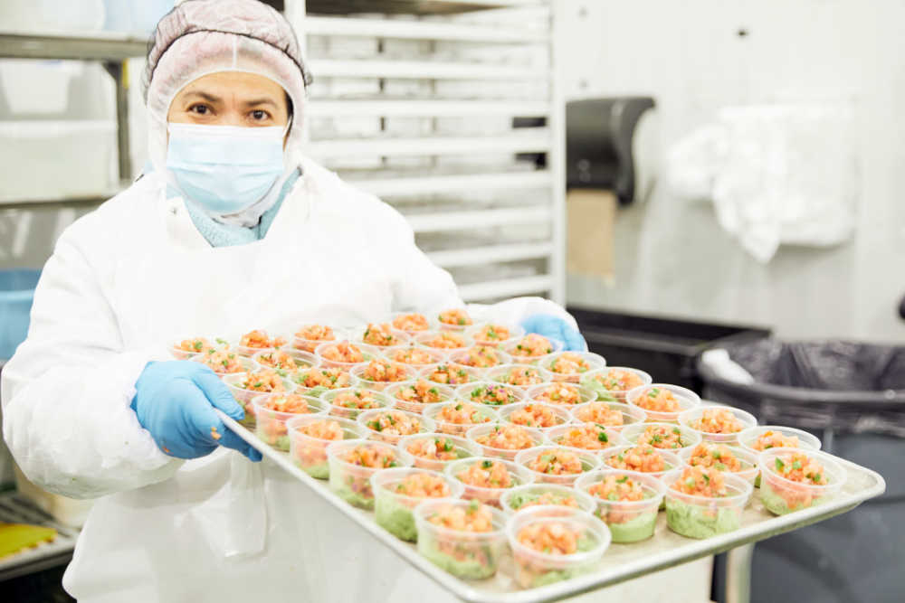 A Farmer's Fridge worker holding up a tray of freshly made salsa and guacamole cups.