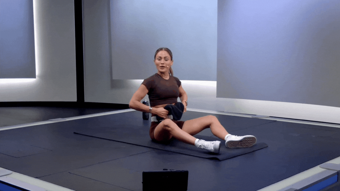 Peloton instructor Olivia Amato demonstrates a Russian twist oblique exercise with a towel during a Peloton core strength class