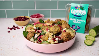 Falafel salad in pink dish with bowls of pomegranate and pickled red onion in the background.