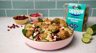 Falafel salad in pink dish with bowls of pomegranate and pickled red onion in the background.