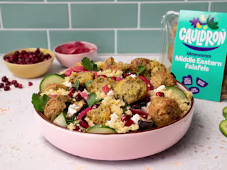 Falafel salad in pink dish with bowls of pomegranate and pickled red onion in the background.
