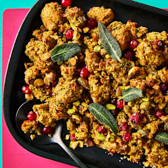 Vegan stuffing in a black serving dish topped with cranberries and sage leaves on a pink and teal background.