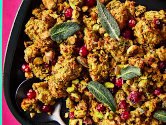 Vegan stuffing in a black serving dish topped with cranberries and sage leaves on a pink and teal background.