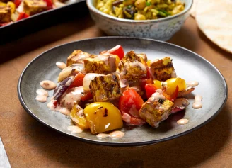 Grilled tofu with pepper and yoghurt dressing on a black plate, with salad in the background.