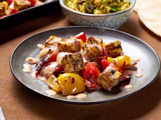 Grilled tofu with pepper and yoghurt dressing on a black plate, with salad in the background.