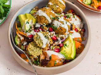 A Carrot Ribbon Salad with Cauldron Middle Eastern Falafels in a bowl with a fork on a cream background.
