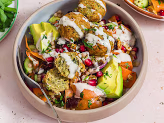 A Carrot Ribbon Salad with Cauldron Middle Eastern Falafels in a bowl with a fork on a cream background.