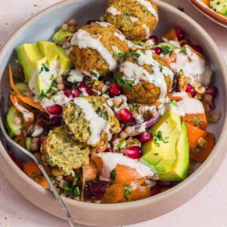 A Carrot Ribbon Salad with Cauldron Middle Eastern Falafels in a bowl with a fork on a cream background.