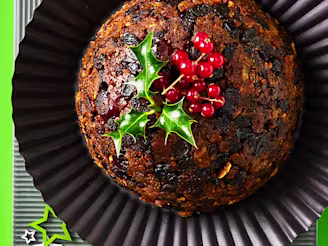 Tofu vegan Christmas pudding topped with holly and berries on a black plate and green background with stars.