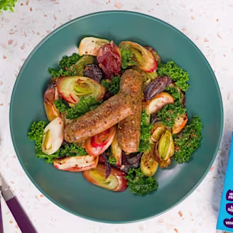 Cauldron Cumberland Sausages with chopped onions, apple and green kale on a blue plate with the blue Cauldron packaging.