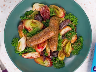 Cauldron Cumberland Sausages with chopped onions, apple and green kale on a blue plate with the blue Cauldron packaging.