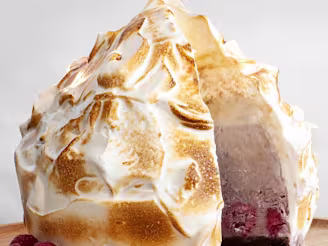 A vegan baked Alaska with a slice removed to showcase the filling with raspberries on the side