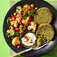 Spinach veggie bakes with a bite taken out of one with roasted cauliflower, broccoli and chickpeas and a dip on the side served in a dark dish with a green background.  