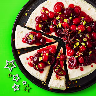 Cheesecake topped with cherries and cranberries on a black plate with a green background and stars. 