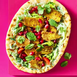 A Tofu Shawarma with yoghurt, tomatoes, cucumber, mint leaves and lettuce on a pink background.