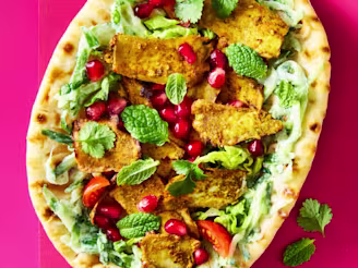 A Tofu Shawarma with yoghurt, tomatoes, cucumber, mint leaves and lettuce on a pink background.