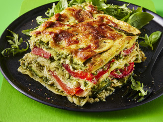 A slice of lasagne with the layers visible to showcase the fillings with a side of rocket served on a dark plate with a green background 