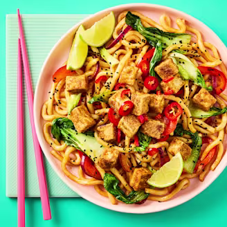 Crispy chilli noodles with Cauldron Tofu Pieces in a pink bowl with pink chopsticks on a teal background.
