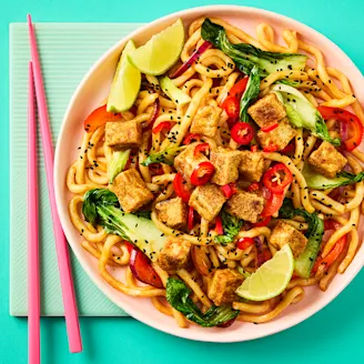 Crispy chilli noodles with Cauldron Tofu Pieces in a pink bowl with pink chopsticks on a teal background.