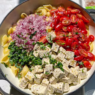 Tofu pasta salad with red onion and tomatoes served in a large dish 