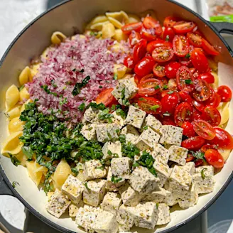 Tofu pasta salad with red onion and tomatoes served in a large dish 