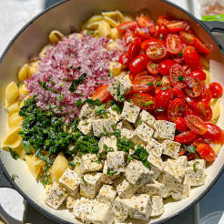 Tofu pasta salad with red onion and tomatoes served in a large dish 