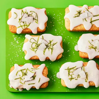 Vibrant green background and serving board with six mini loaves topped with white icing and lime zest.