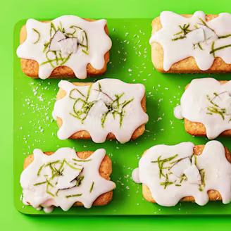 Vibrant green background and serving board with six mini loaves topped with white icing and lime zest.