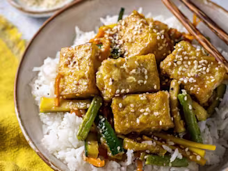 Sticky Teriyaki Tofu served on a bed of rice and vegetables in a white bowl and chopsticks on the side