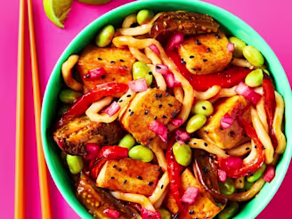 Tofu & Aubergine Miso Yaki Udon served in a bowl with chopsticks and a wedge of lime on the side.