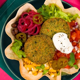 Blue plate with tortilla holding two veggie bakes, diced red onion, greens, jalapenos, tomatoes and corn. Green Cauldron packaging on the right.