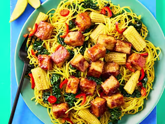 Cauldron Tofu Pieces in a soy and garlic sauce with Singapore noodles and chopped vegetables on a green plate with black cutlery.