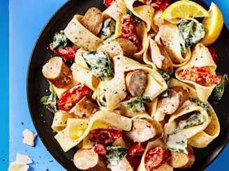 Cauldron Cumberland sausages and pasta with vegetables served in a dark dish with lemon slices on the side, the background is blue