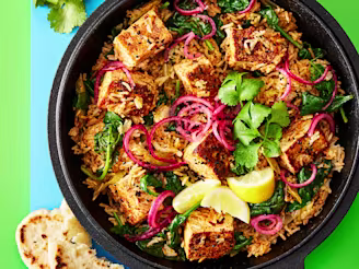 Biryani made using Cauldron Tofu topped with red onion, coriander and lemon slices served in a large dark pot with a green background