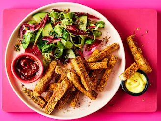 A pink plate with tofu fries and a side salad with two pots of dip on a pink background.