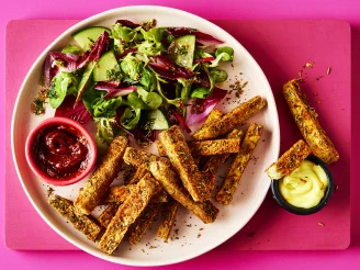 A pink plate with tofu fries and a side salad with two pots of dip on a pink background.