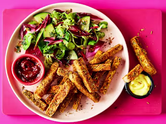 A pink plate with tofu fries and a side salad with two pots of dip on a pink background.