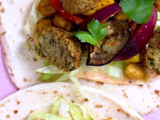 Cauldron Middle Eastern Falafels with onion, pepper, lettuce and chickpeas on two tortillas on a pink background.