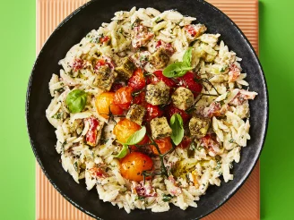 Orzo pasta in a black bowl topped with vine tomatoes, croutons and basil garnish.