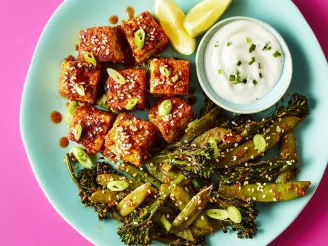 Tofu in buffalo sauce on blue plate with tenderstem broccoli, ranch dipping sauce and lemon wedges, on pink background.