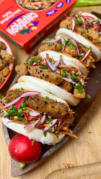 Four bao buns with Marinated Tofu and rainbow slaw filling. Red Cauldron Marinated Tofu packaging in the background. 