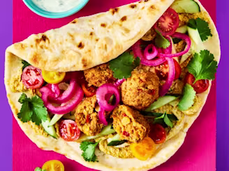 Pita with Cauldron Butternut and Red Chilli bites, chopped cherry tomatoes, coriander, pickled red onion and a side dish of yoghurt dip on a vibrant pink and purple background.
