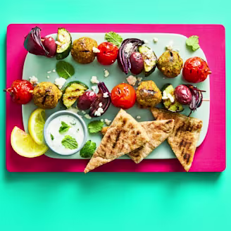Greek falafel skewers with Cauldron Middle Eastern Falafels on teal plate on a pink board.