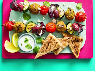 Greek falafel skewers with Cauldron Middle Eastern Falafels on teal plate on a pink board.