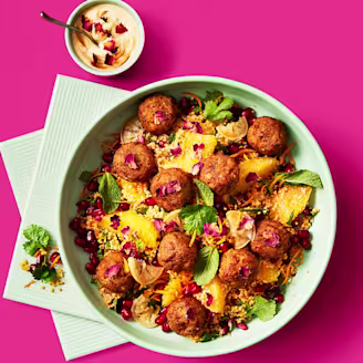 Moroccan falafels served on top of vegetarian couscous topped with pomegranate seeds in a blue bowl and a sauce on the side 